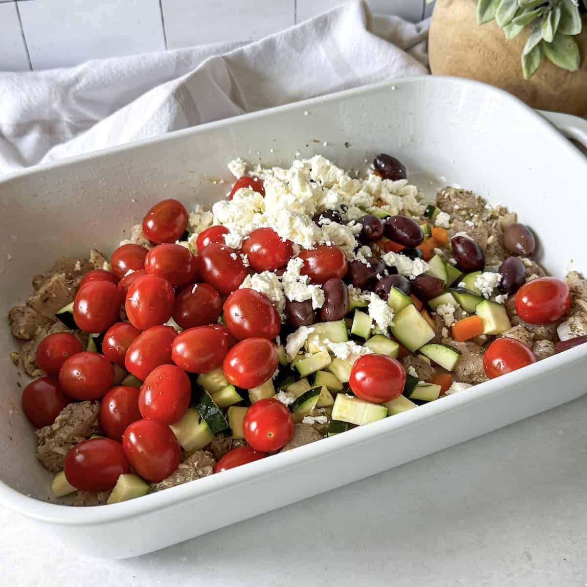 vegetables and feta cheese on top of seasoned chicken in a baking dish.
