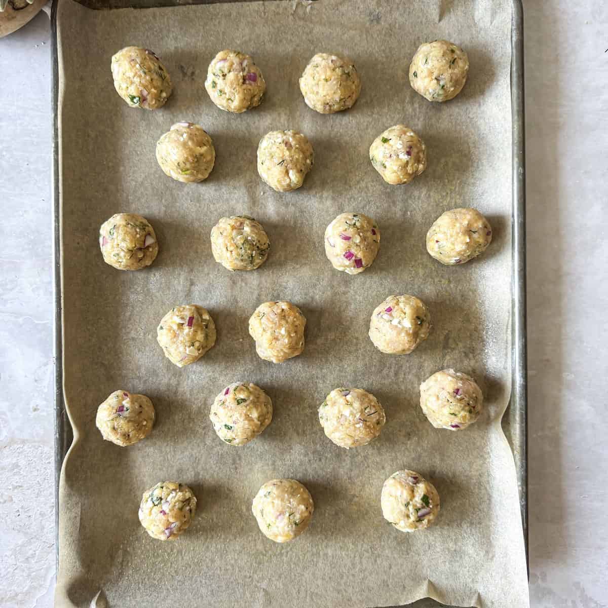 greek chicken meatballs raw on a baking sheet lined with parchment paper.