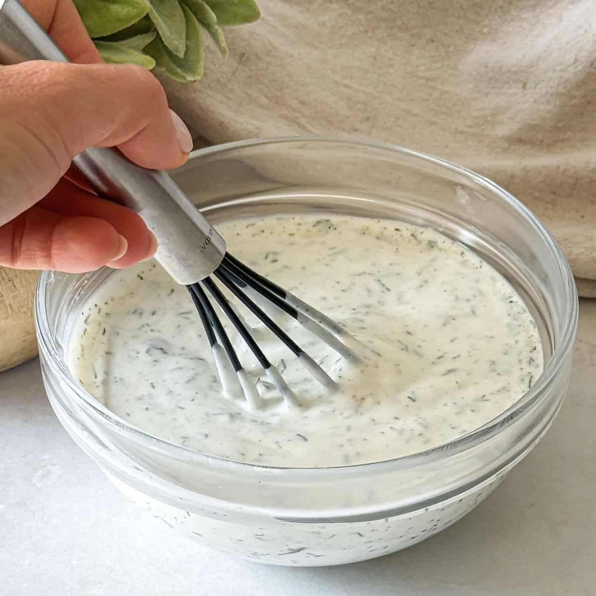 hand whisking greek yogurt dill sauce.
