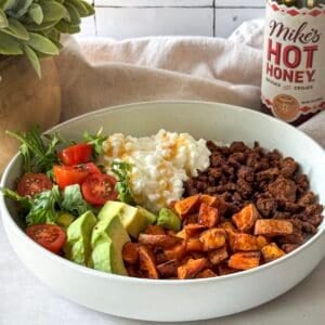 hot honey ground beef bowl with cottage cheese and sweet potatoes in a bowl with a bottle of mike's hot honey behind it.
