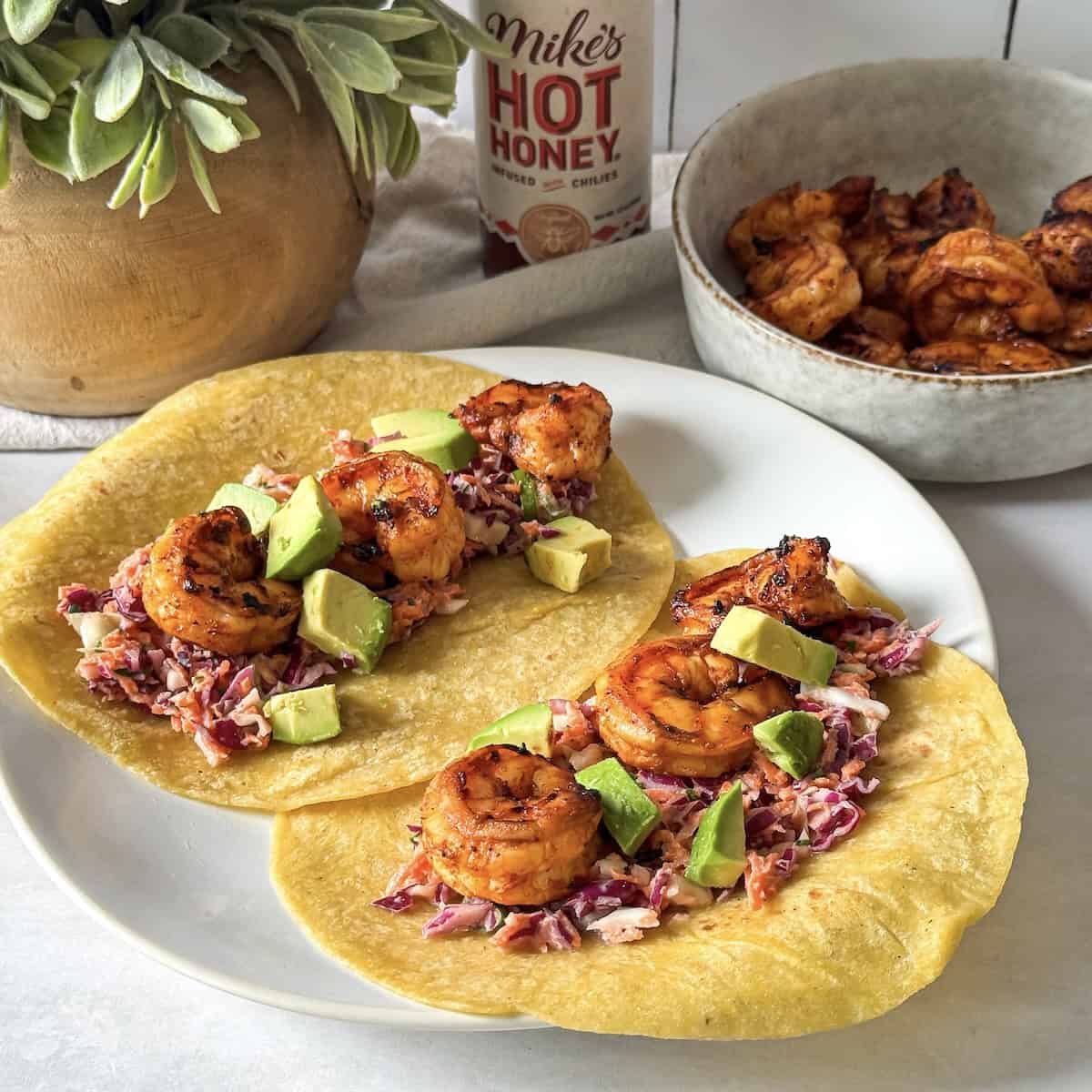 hot honey shrimp taocs with Mike's hot honey in the background on a plate.