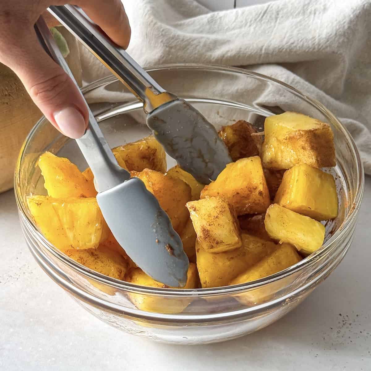 human hand tossing pineapple chunks in cinnamon and honey.