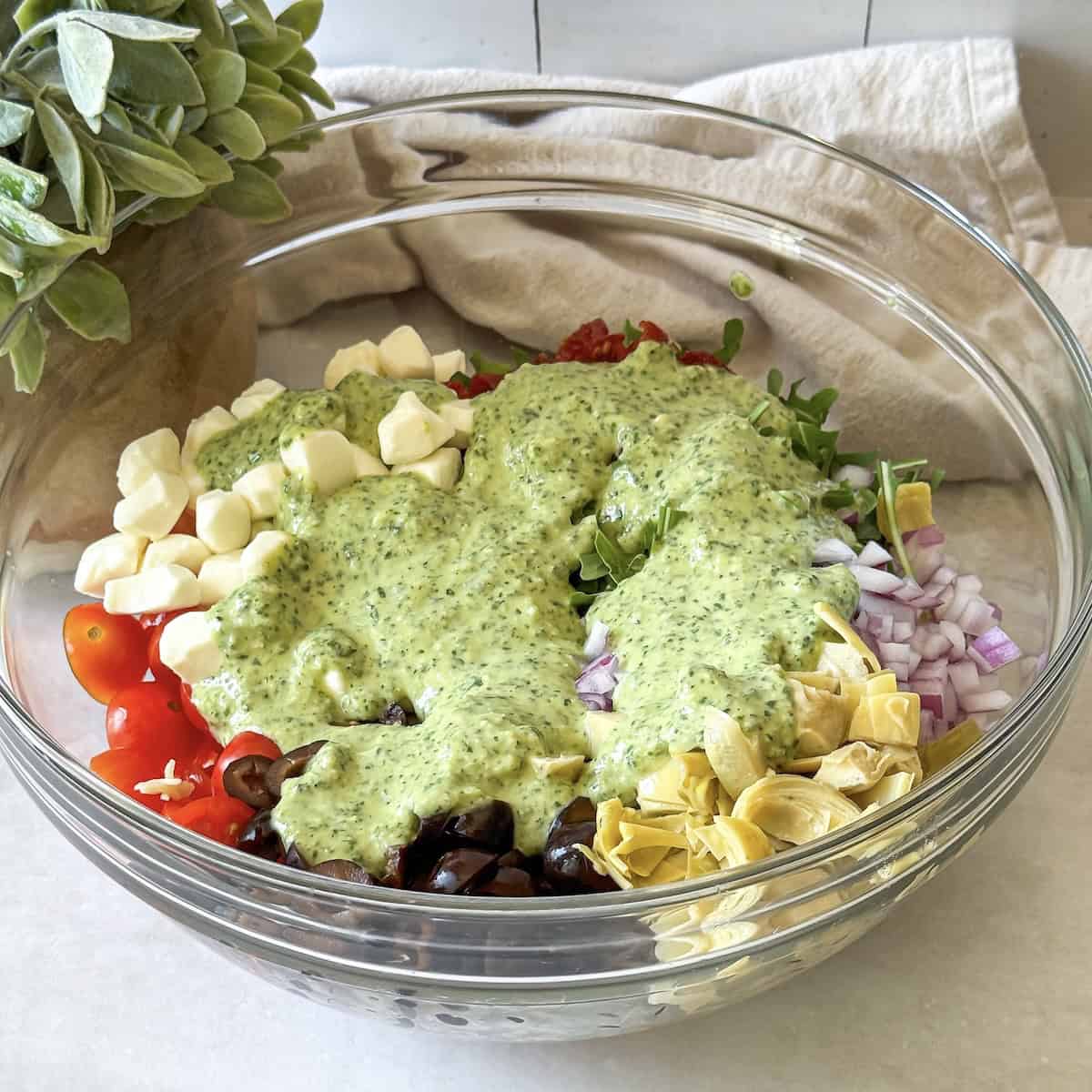 ingredients for pesto pasta salad in a glass bowl with pesto poured on top.