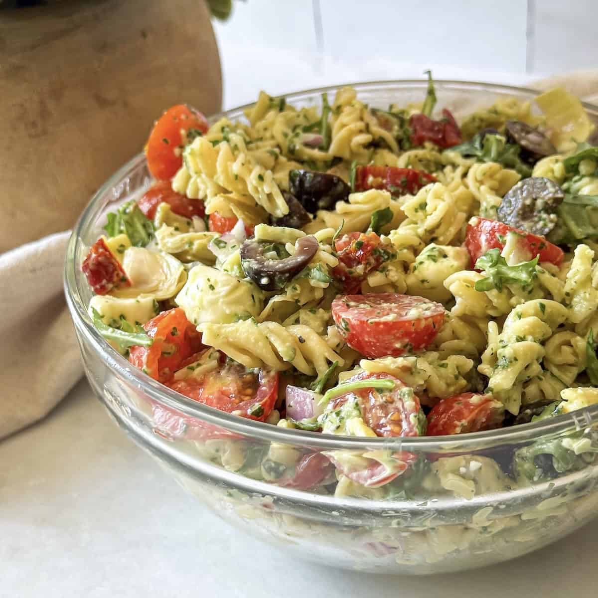 ingredients for pesto pasta salad with sundried tomatoes in a glass bowl side view.