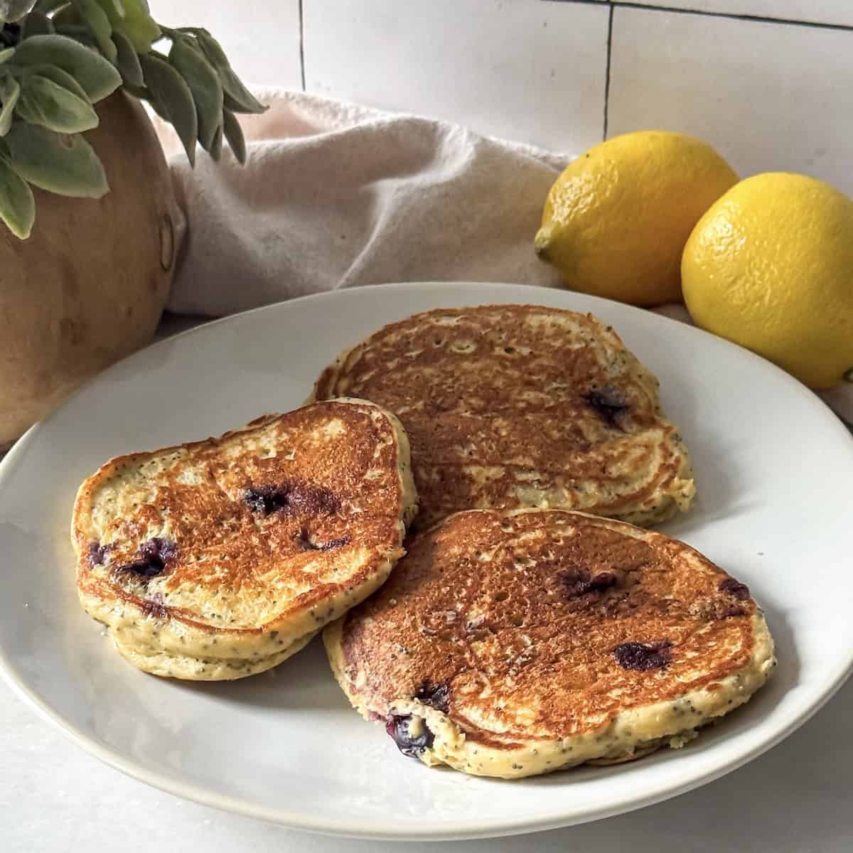 lemon poppy seed pancakes on a plate with lemons in the background.