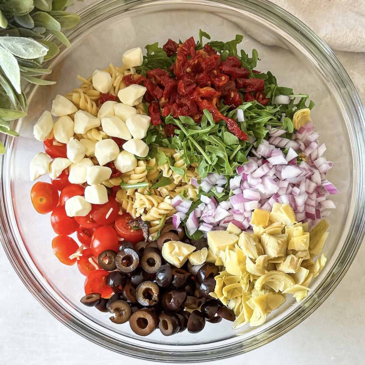 overhead view of pesto pasta salad ingredients in a glass bowl.
