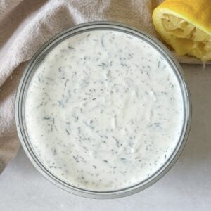 overhead view of yogurt dill sauce in a glass bowl with a lemon in the background.