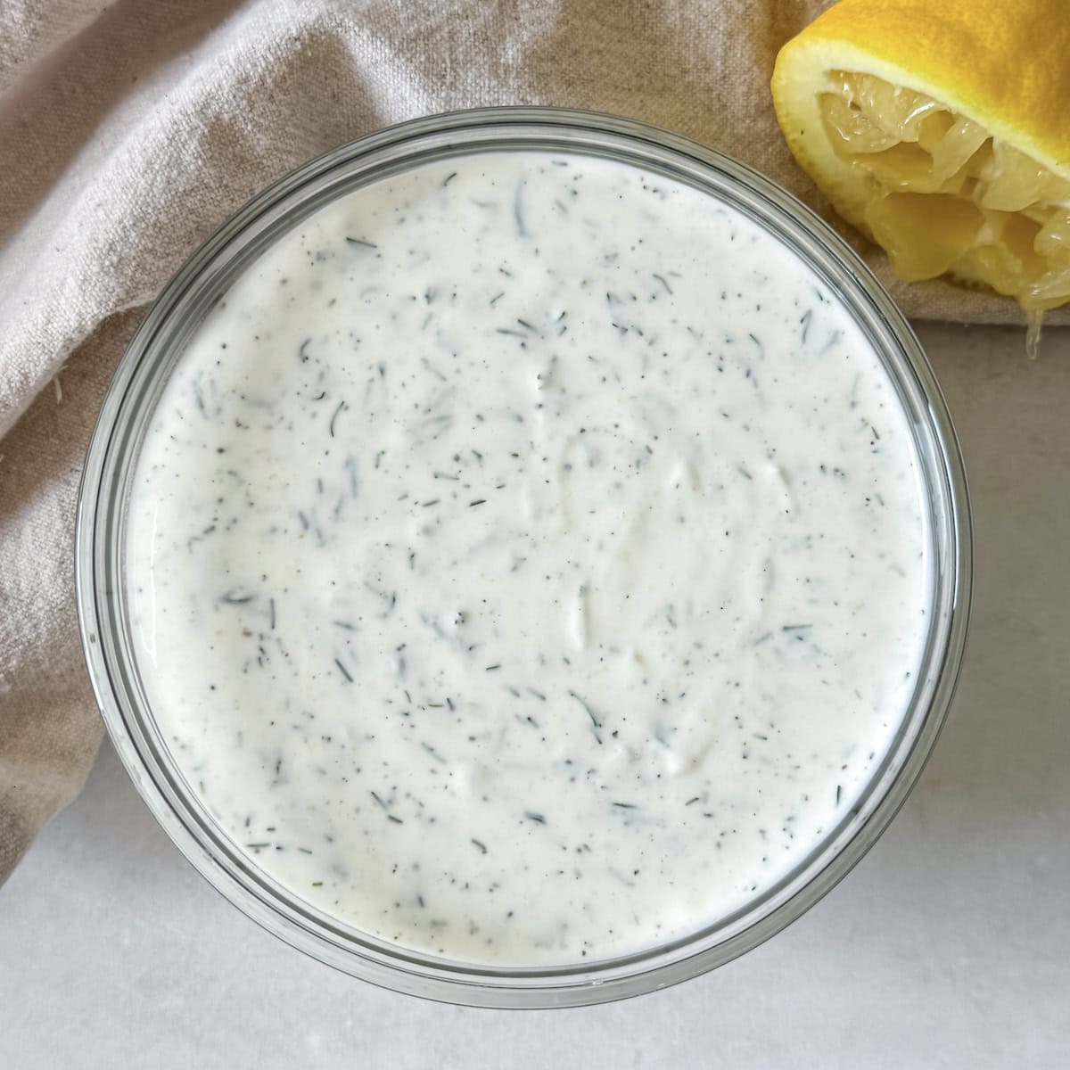 overhead view of yogurt dill sauce in a glass bowl with a lemon in the background.
