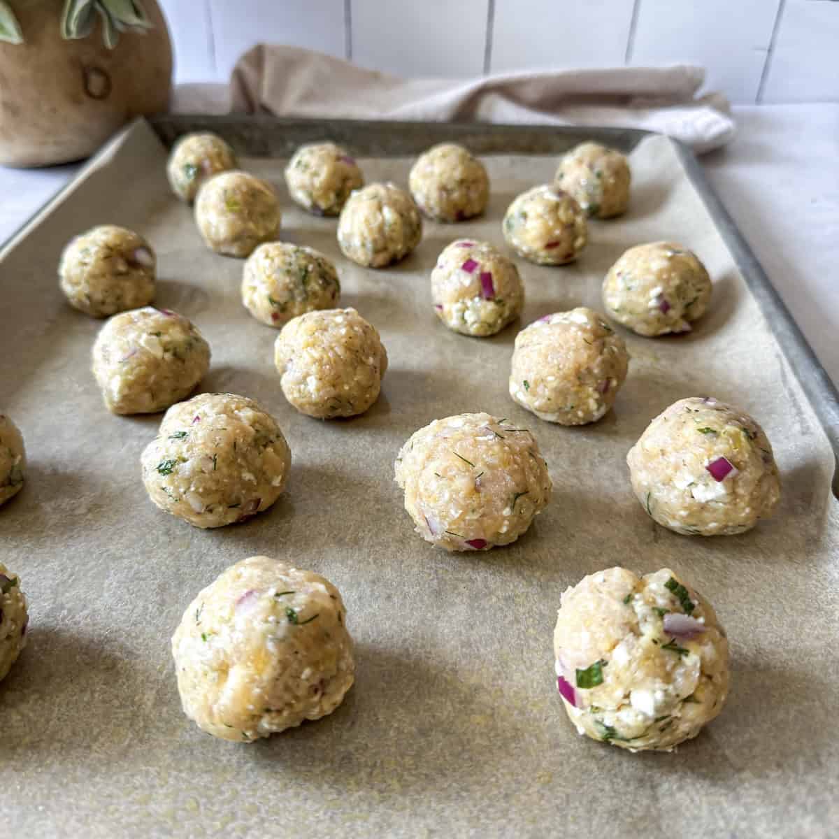 raw greek chicken meatballs on a baking sheet.