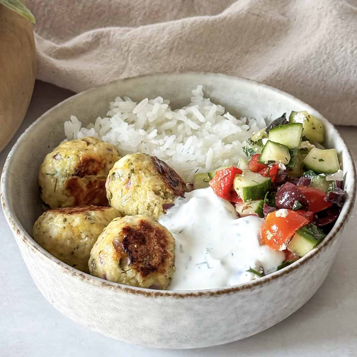 side view of greek chicken meatball bowl wiht yogurt dill sauce.