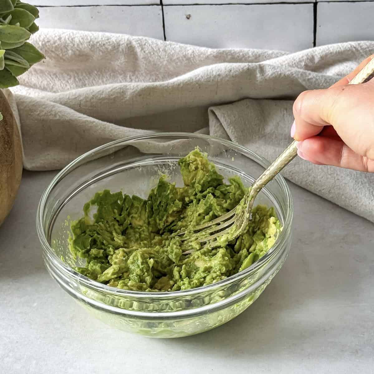 a human hand mashing an avocado.