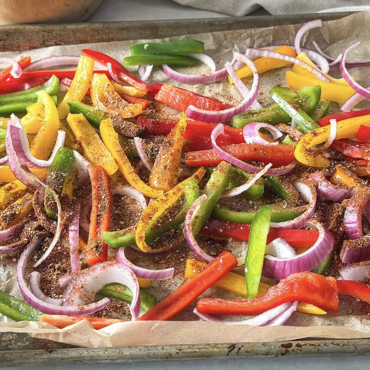 bell peppers and red onion sliced on a baking sheet with seasonings.