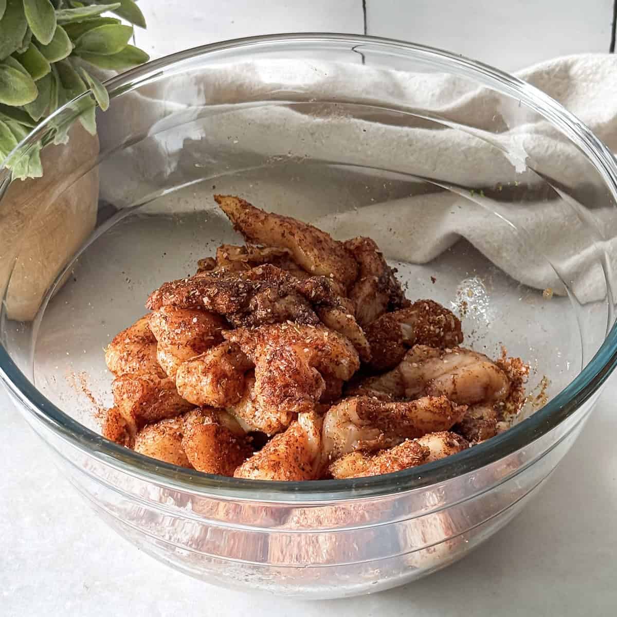 chicken marinading in seasonings and olive oil in a glass bowl.