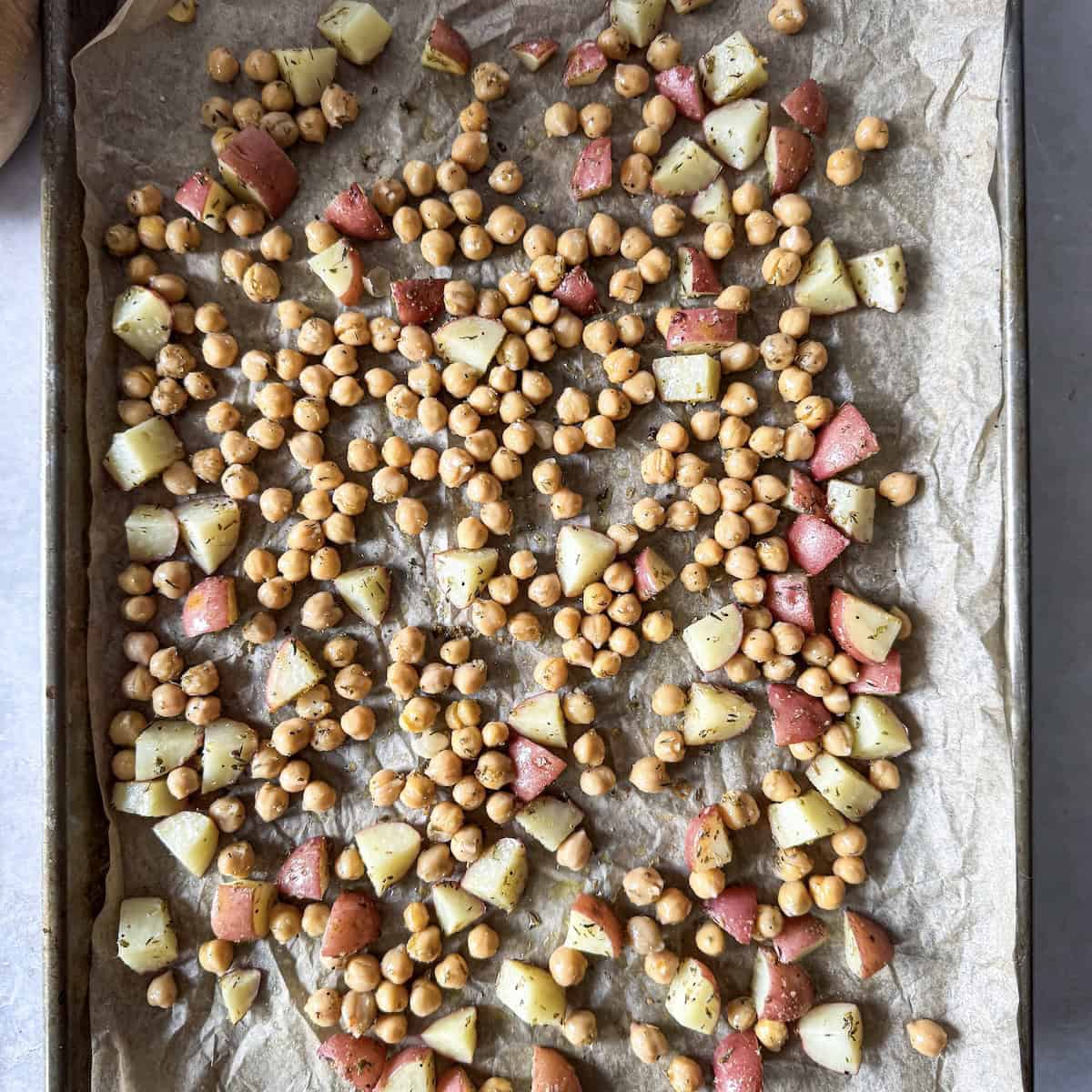chickpeas added to a baking sheet with potatoes.