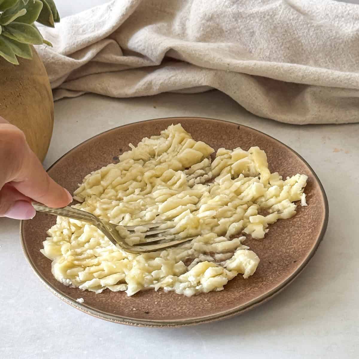 human hand holding a fork mashing a banana.