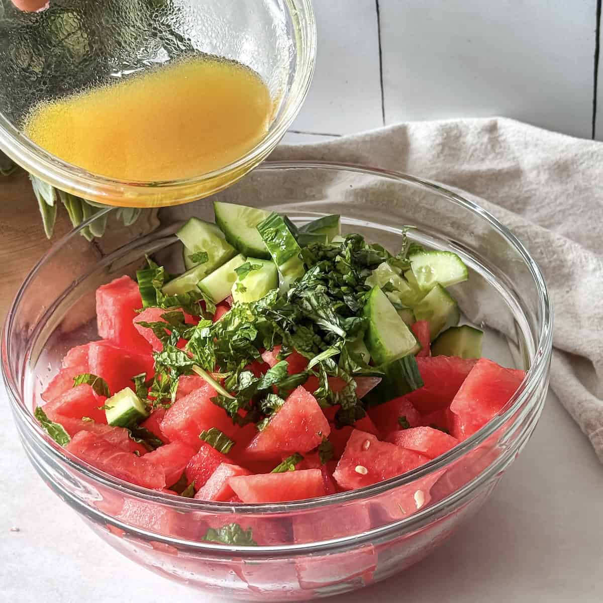 human hand pouring dressing on watermelon cucumber salad.