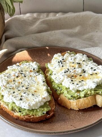 side view of avocado cottage cheese toast on a brown plate.