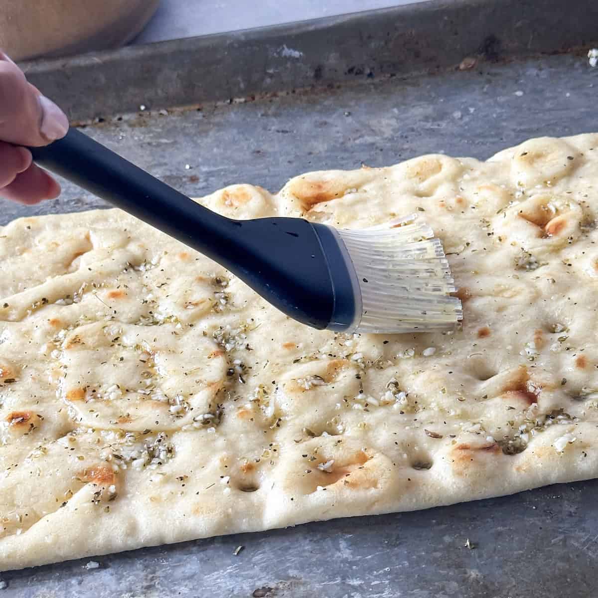a human hand brushing flatbread with olive oil.