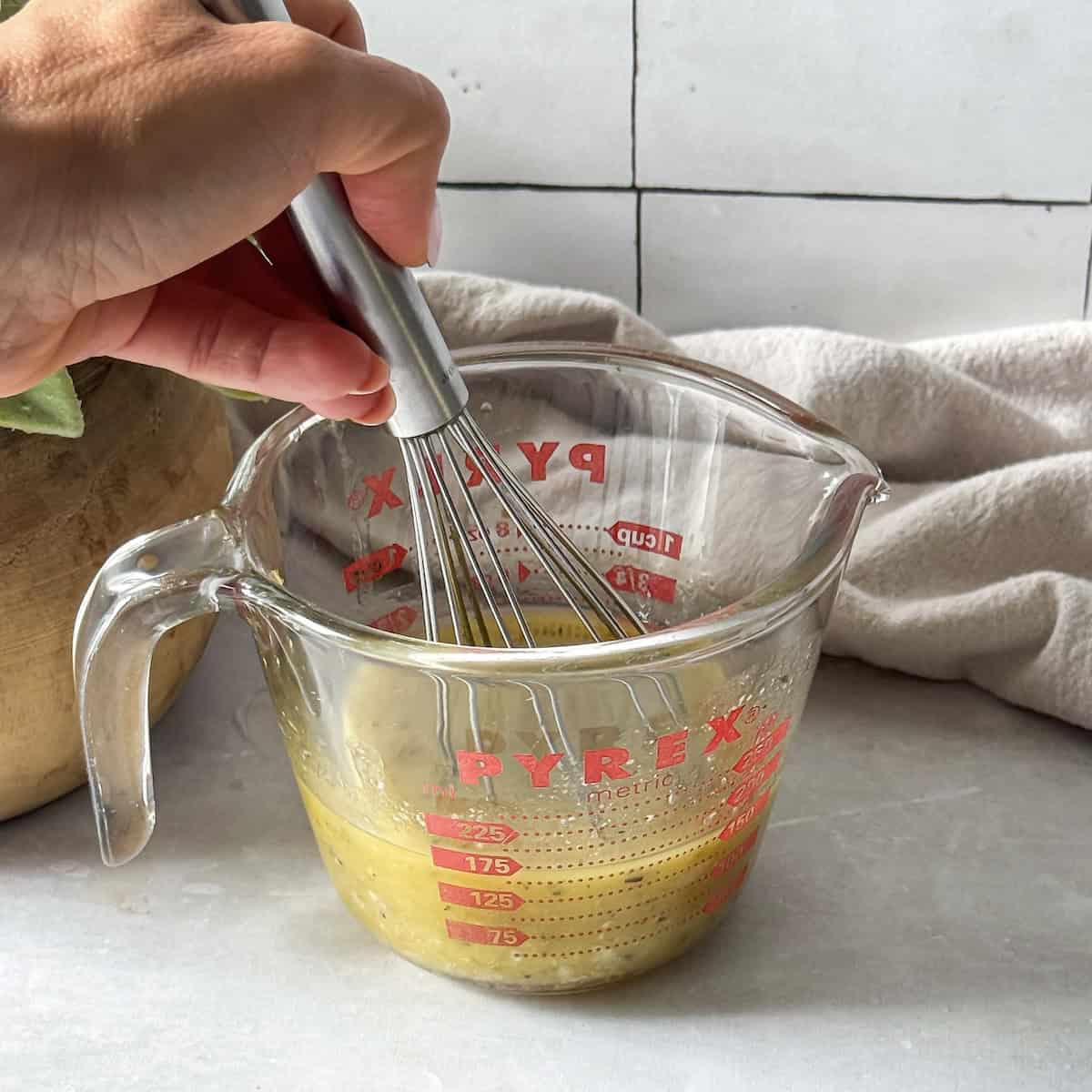 human hand whisking honey lemon salad dressing.
