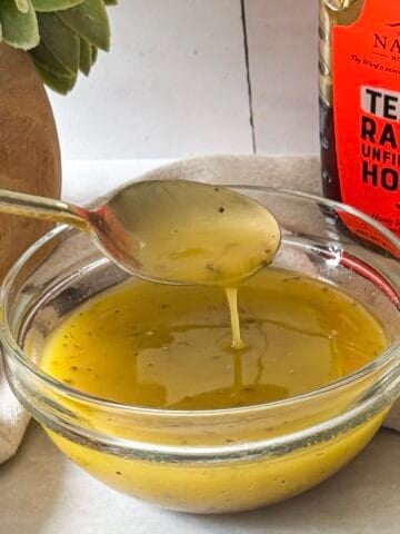 side view of honey lemon dressing with a spoon.