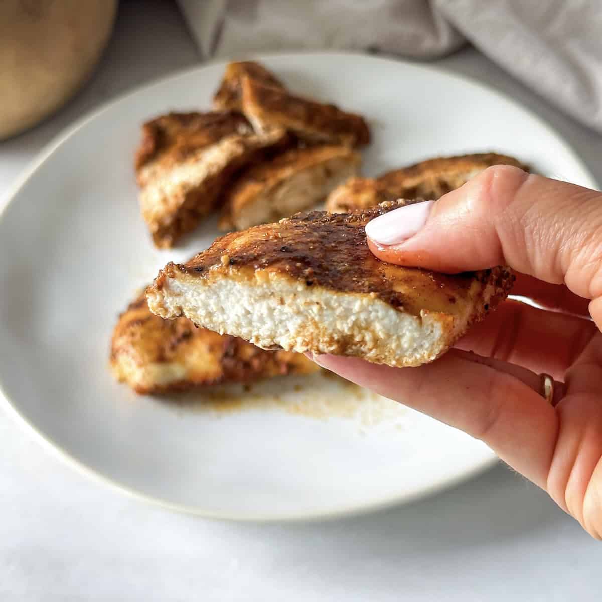 a hand holding baked thinly sliced chicken breast.