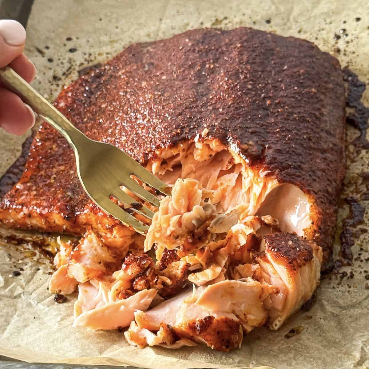 human hand holding a fork taking a bite of smoked paprika salmon.