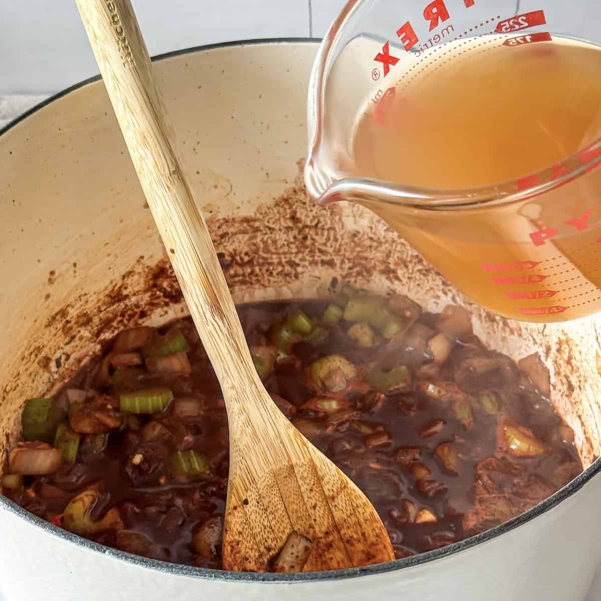 human hand pouring broth into beef stew.