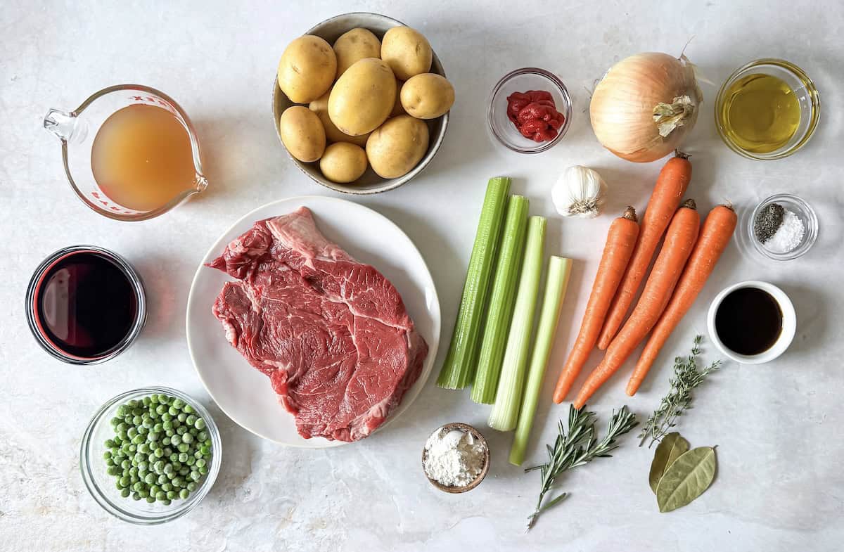 ingredients for beef stew with carrots and potatoes on a table.