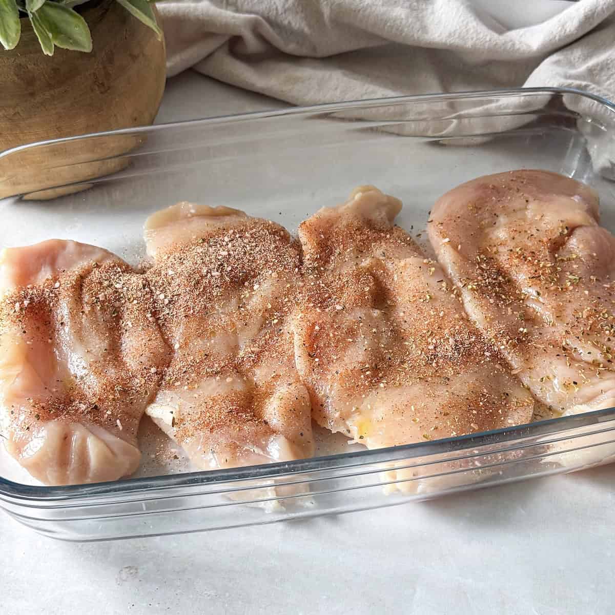 seasoning added to chicken breast in a glass baking dish.