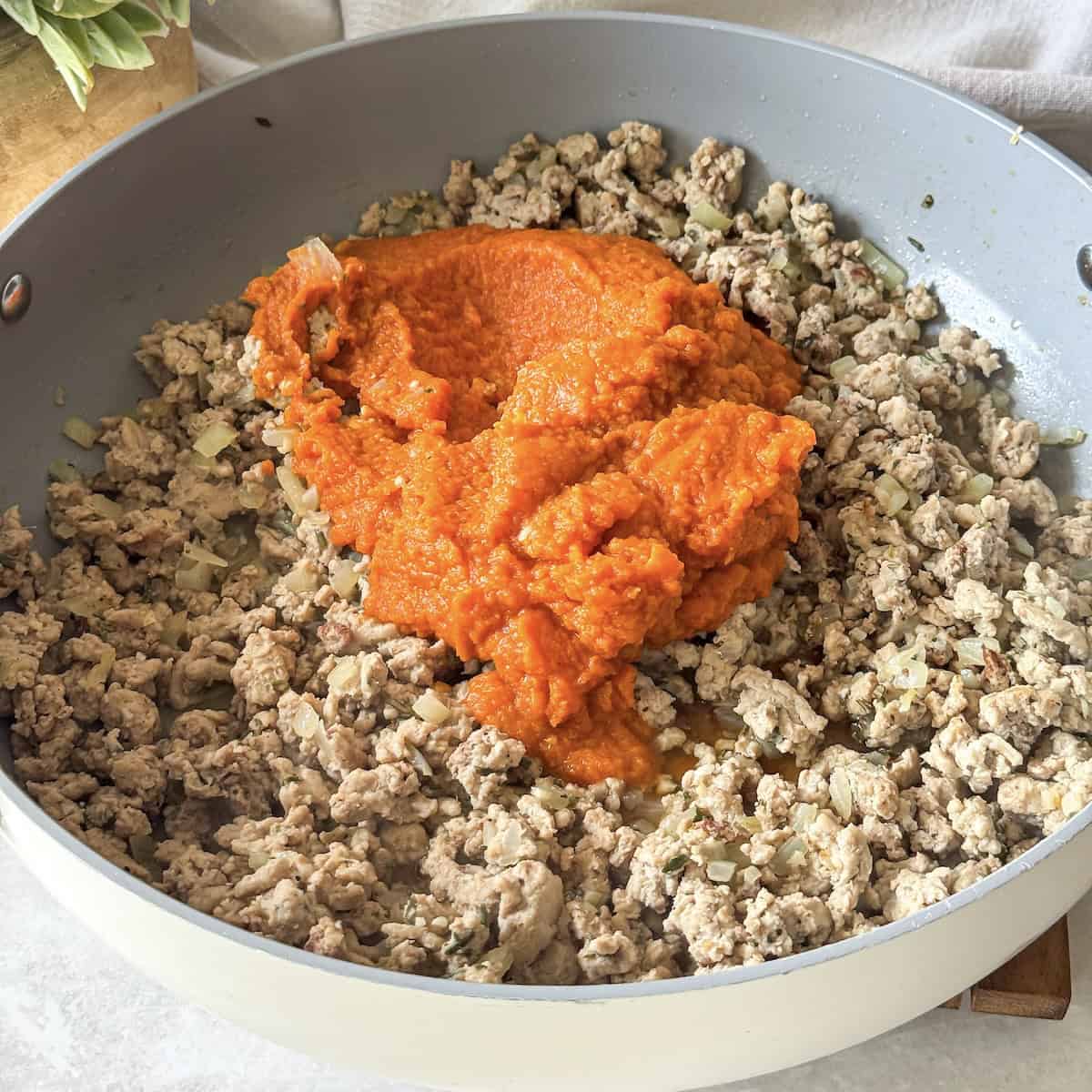 pumpkin and chicken broth added to a skillet with turkey.