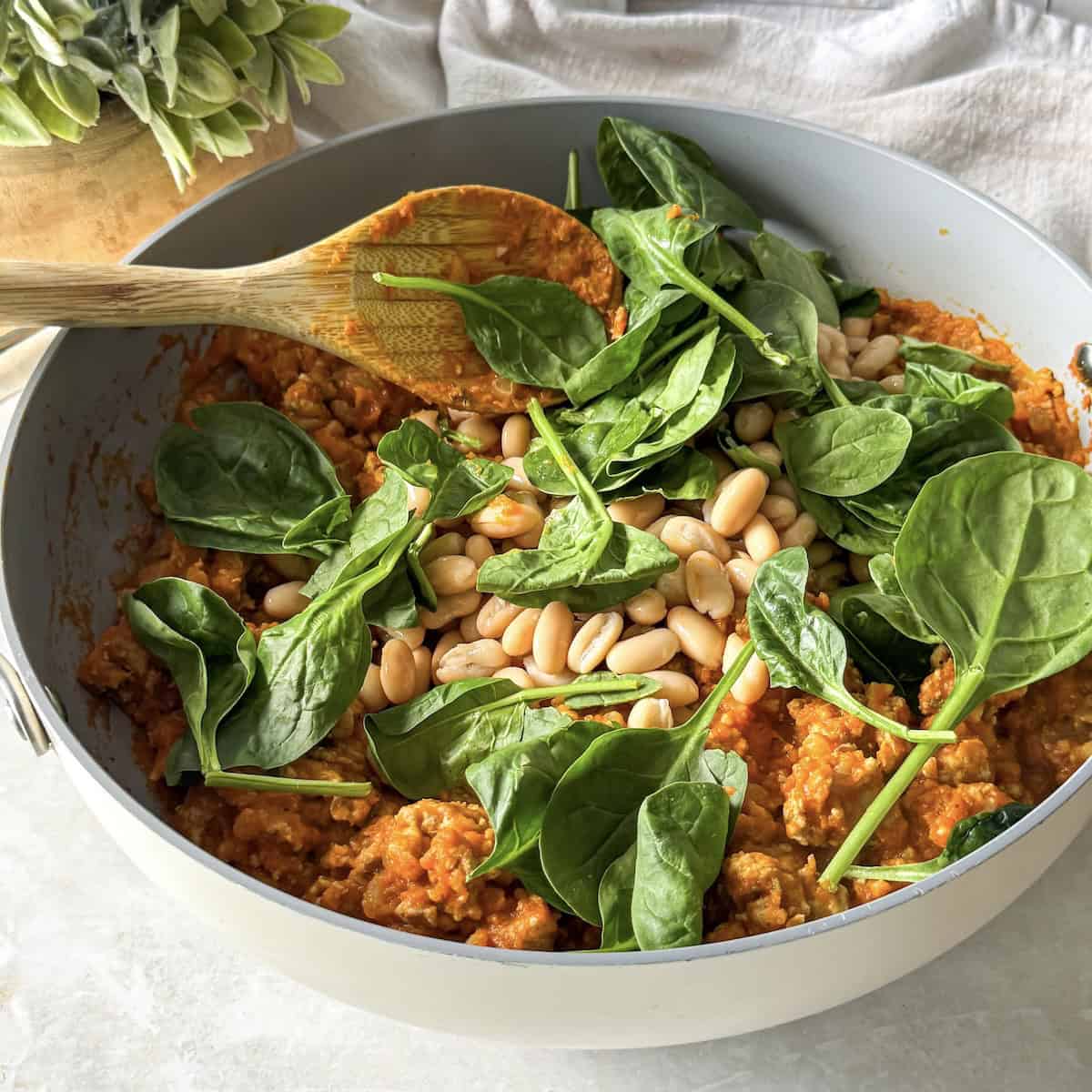 spinach and white beans added to a skillet with turkey and pumpkin.