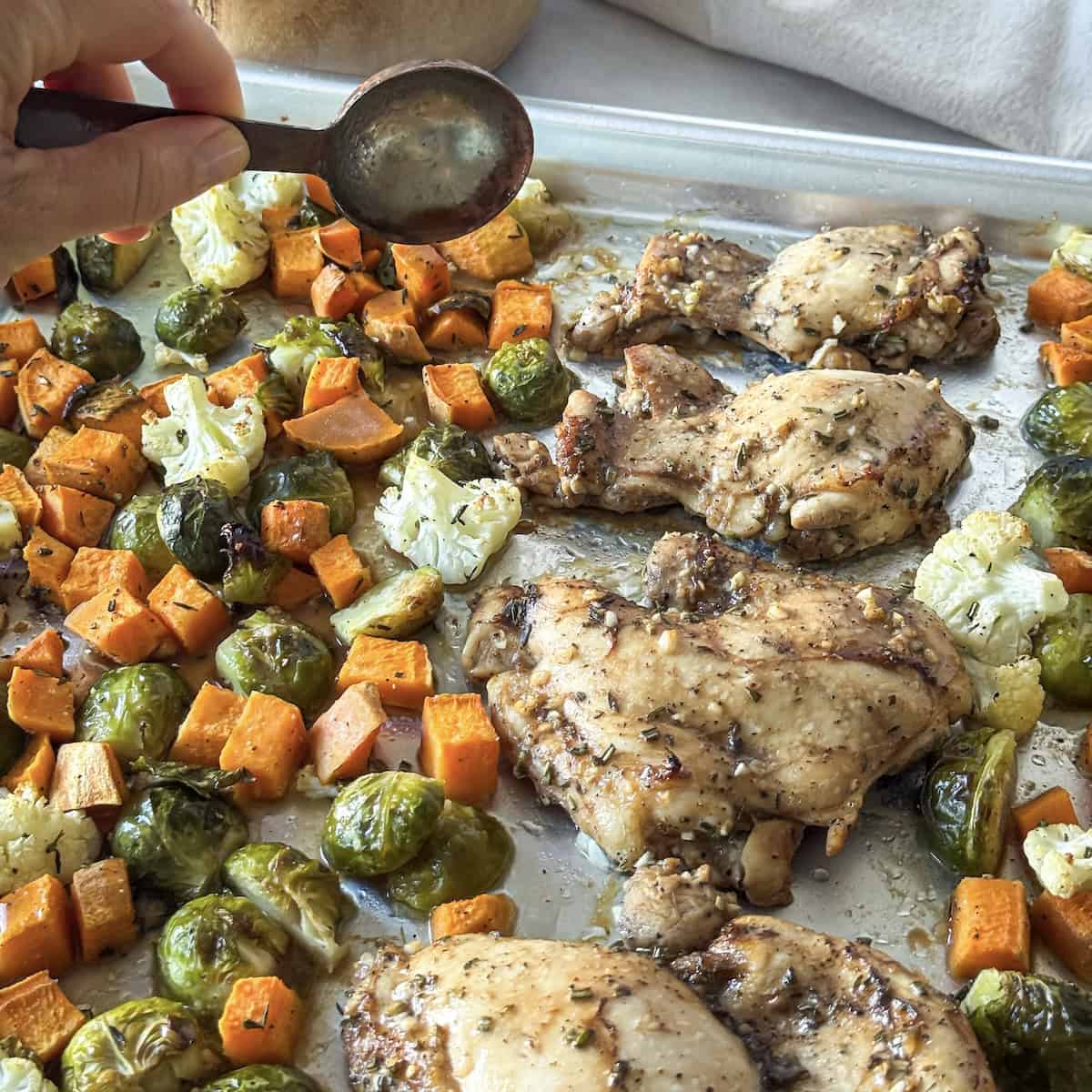 human hand pouring maple balsamic dressing on chicken thigh sheet pan dinner.
