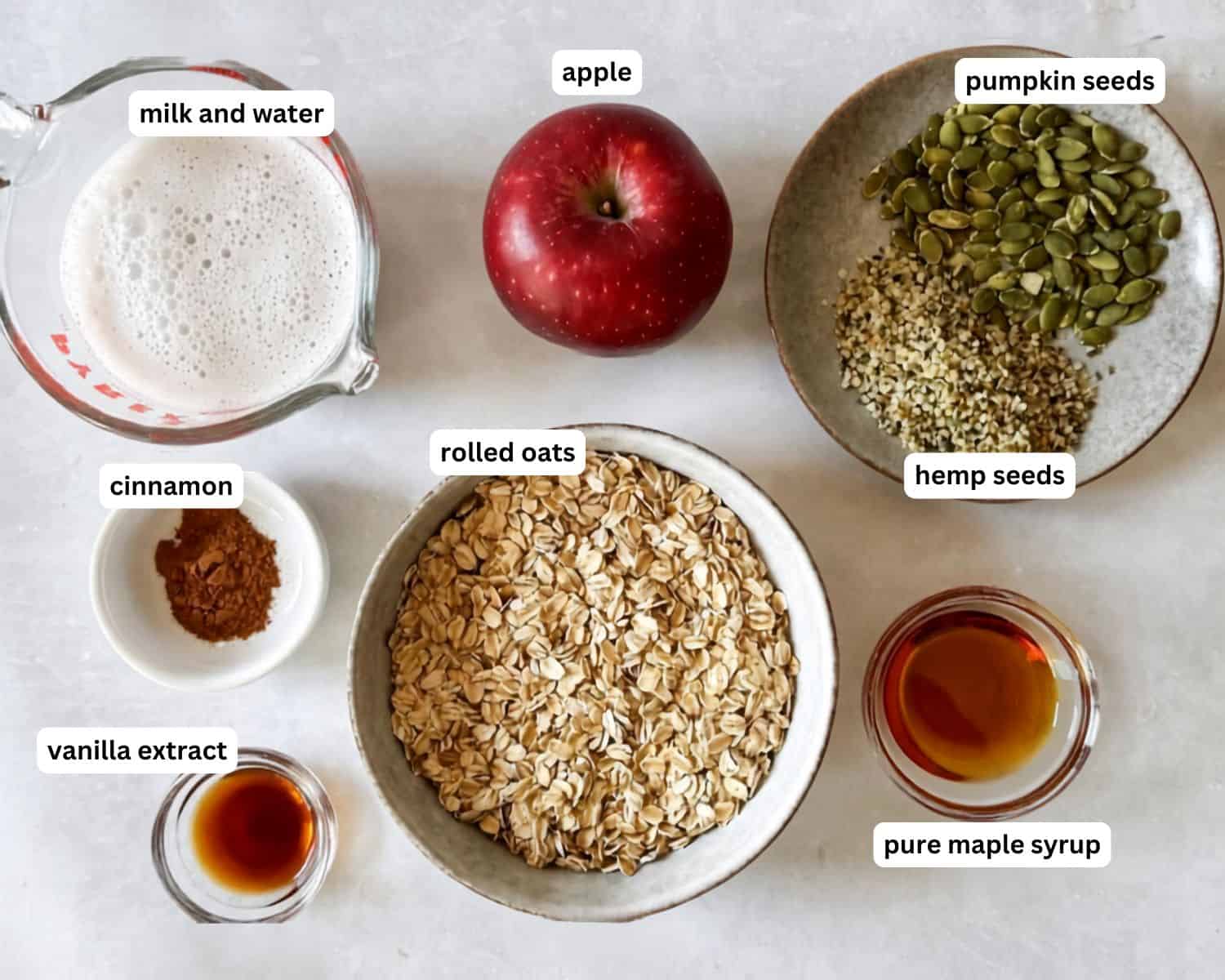ingredients for apple cinnamon oatmeal in separate containers on a table with a grayish white background.