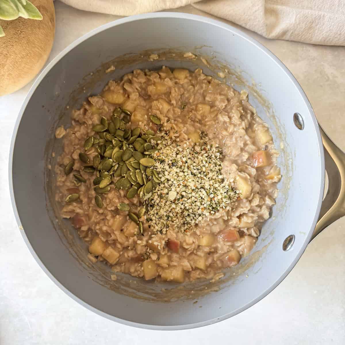 overhead view of apple cinnamon oatmeal in a saucepan with hemp seeds and pumpkin seeds added to it.