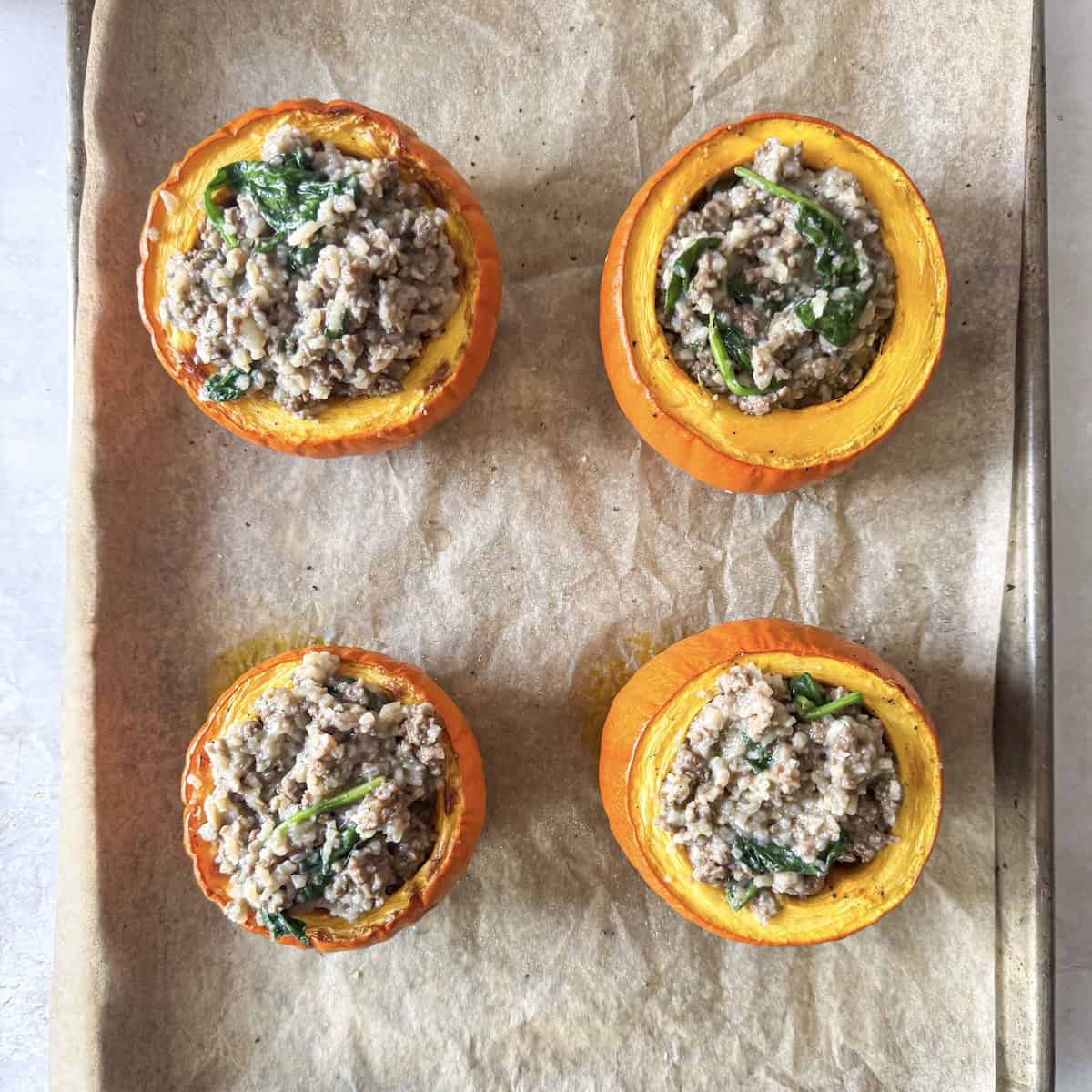 overhead view of stuffed pumpkins on a baking sheet before cheese is added to the top.