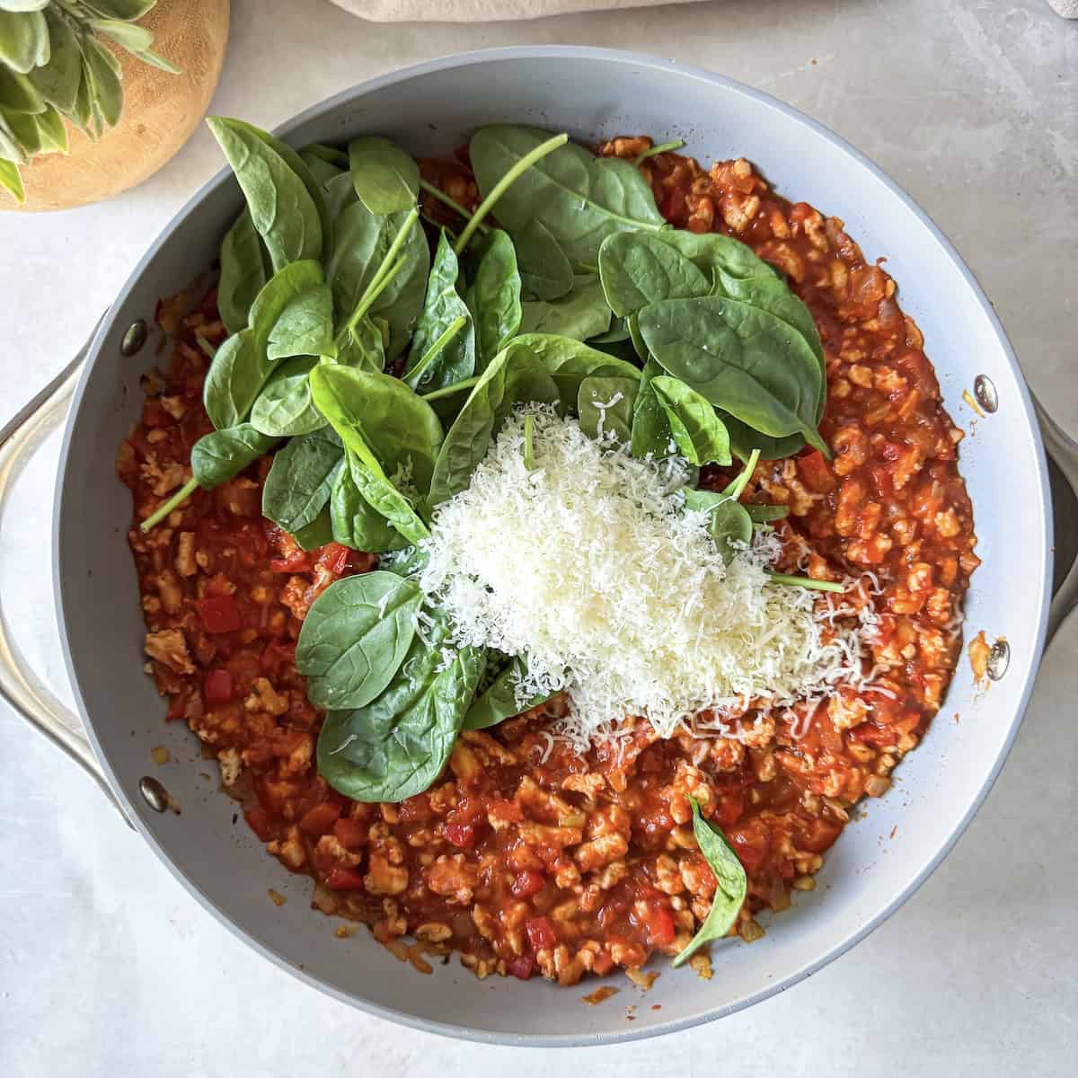 overhead view of turkey, marinara sauce, spinach, and cheese in a skillet.