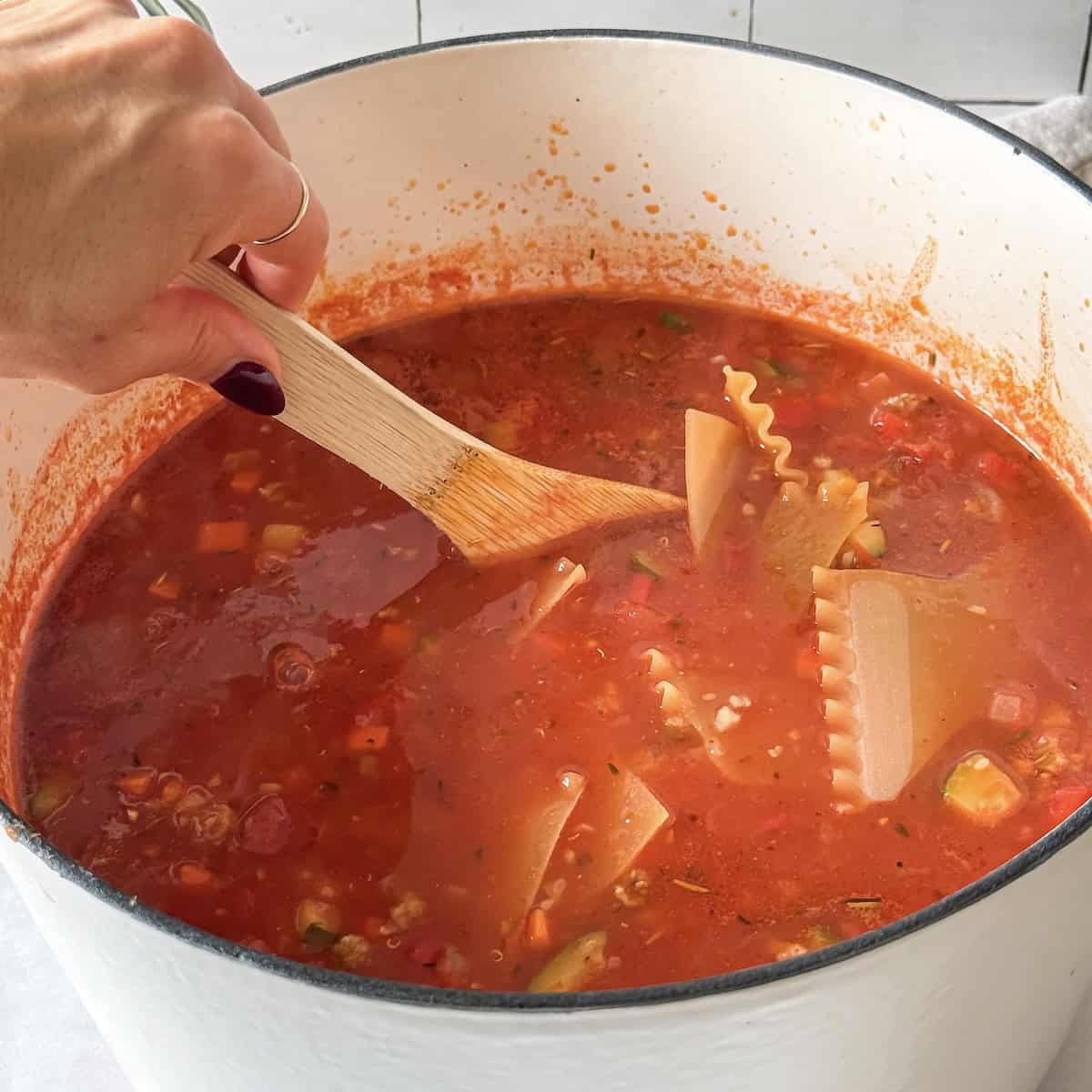 human hand stirring lasagna noodles in a pot.