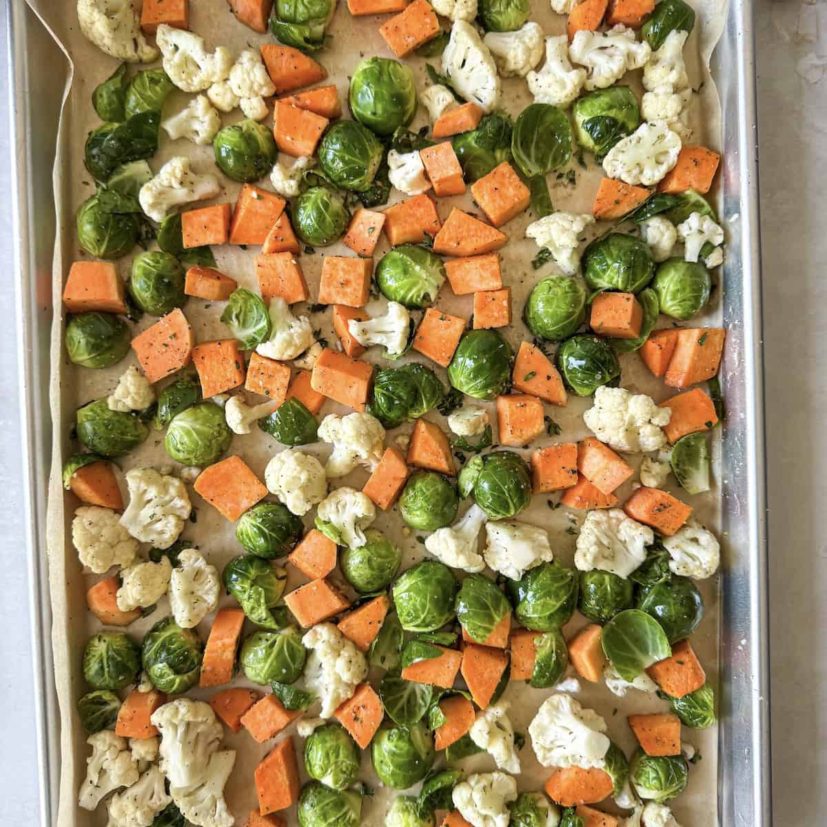 overhead view of brussels, sweet potatoes, and cauliflower on a sheet pan.