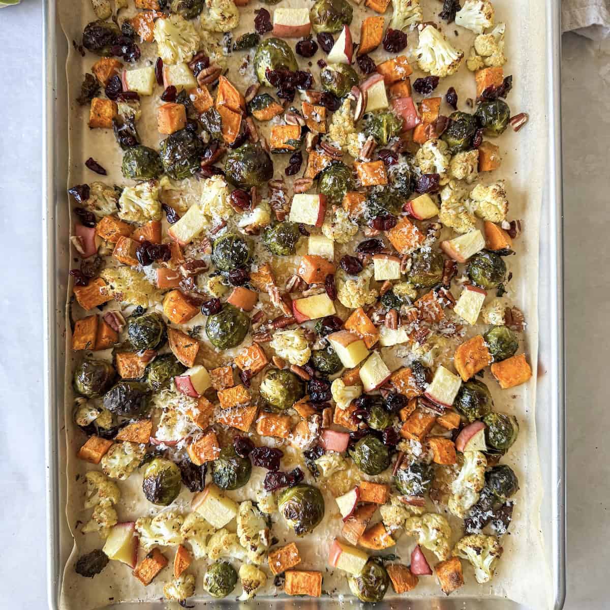 overhead view of roasted brussels sprouts and sweet potatoes with cranberries and pecans on a sheet pan.