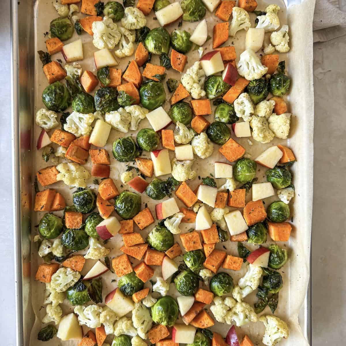 overhead view of sweet potatoes, brussels, cauliflower, and apple on a sheet pan.