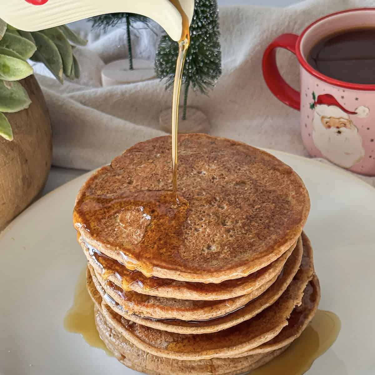a human hand pouring maple syrup on top of a stack of gingerbread pancakes.