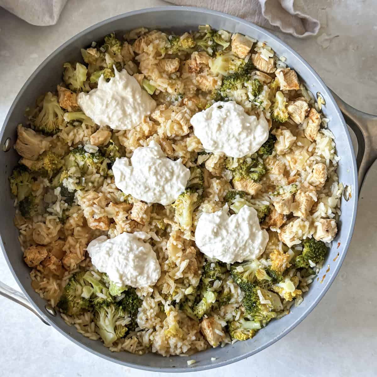 overhead view of cheese and greek yogurt added to a broccoli chicken rice skillet.