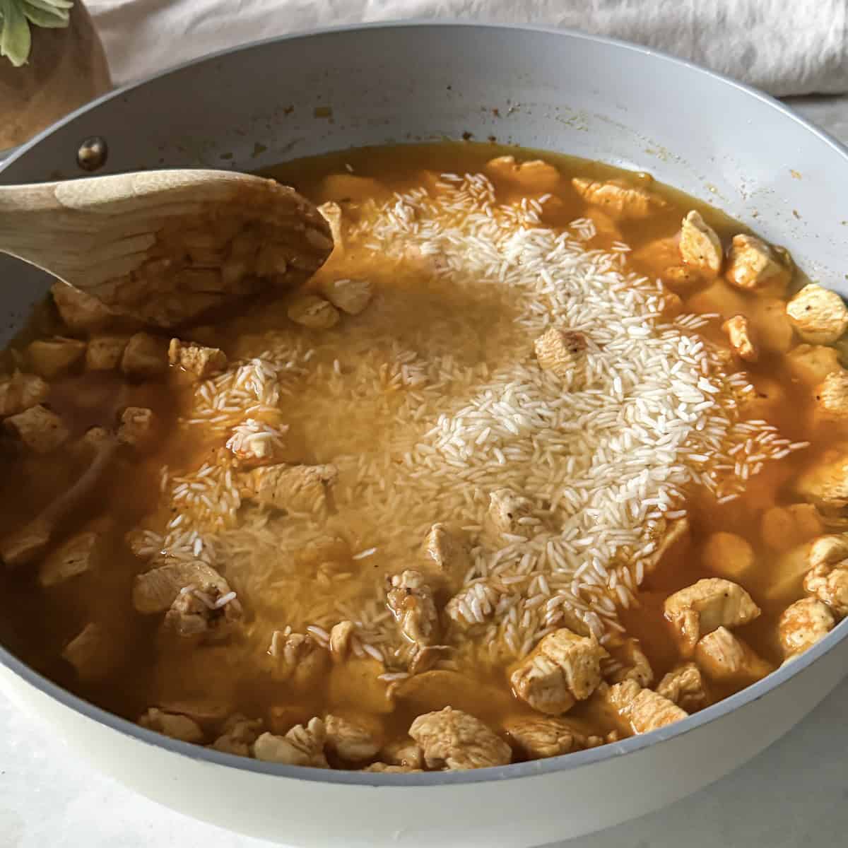 rice and chicken broth added to a skillet with chicken.