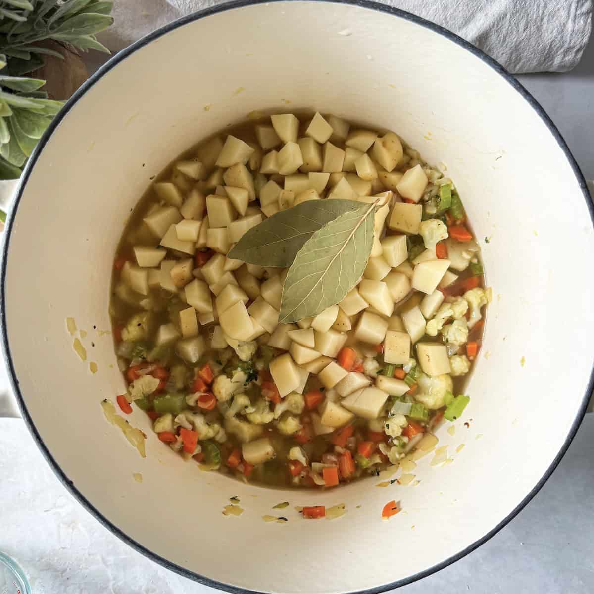bay leaves added to chicken pot pie soup ingredients in a Dutch oven.