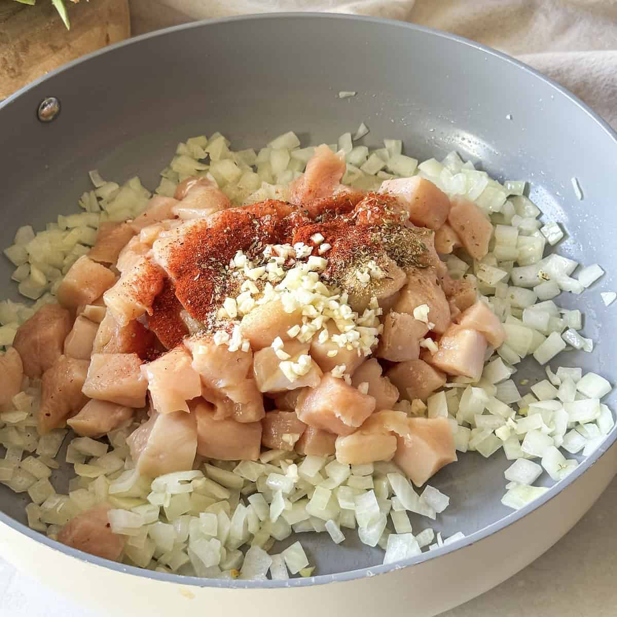 chicken, garlic, and seasonings added to onions in a skillet.