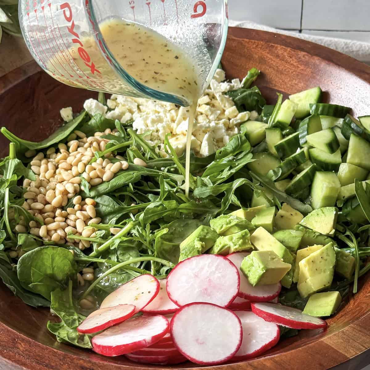 dressing being poured on a spinach and arugula salad.
