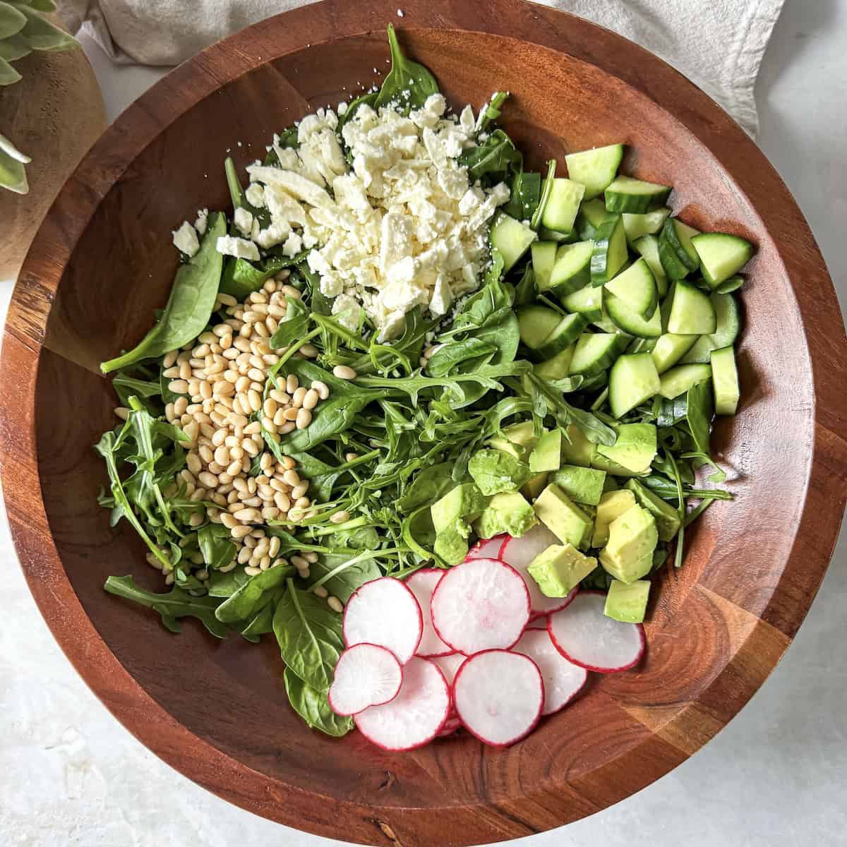 overhead view of ingredients for spinach and arugula salad in a wooden salad bowl..