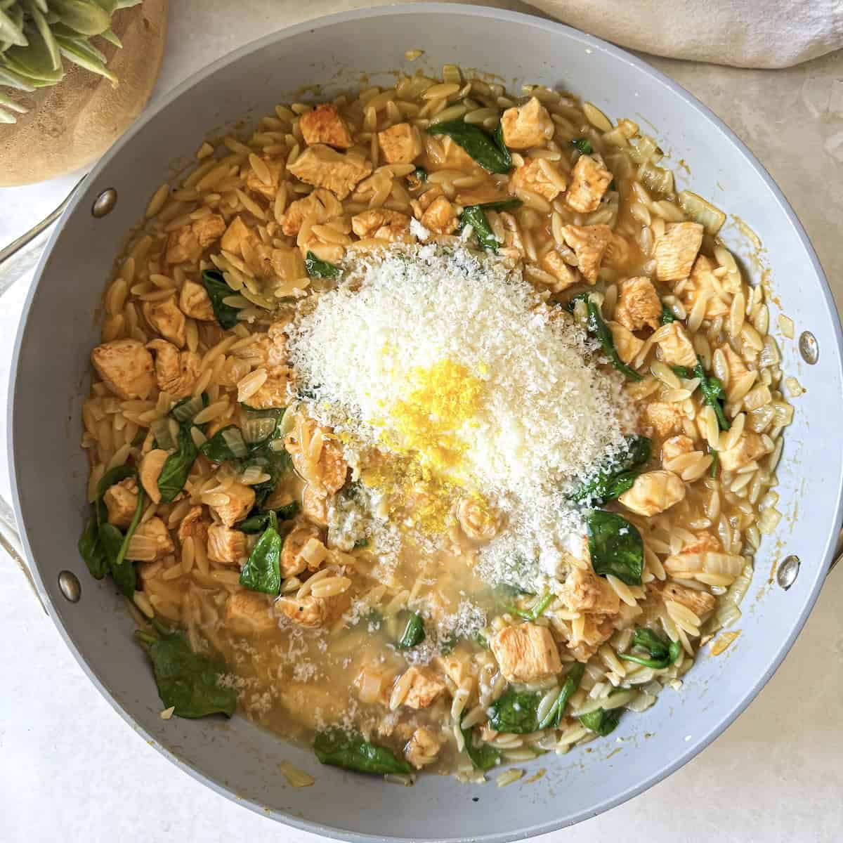overhead view of parmesan and lemon zest in a skillet with chicken and orzo pasta.