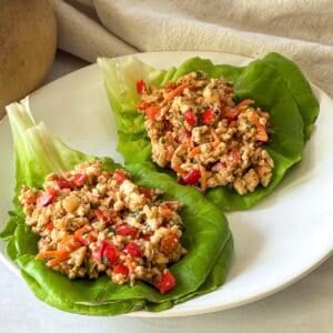 side view of 2 thai chicken lettuce wraps on a plate.