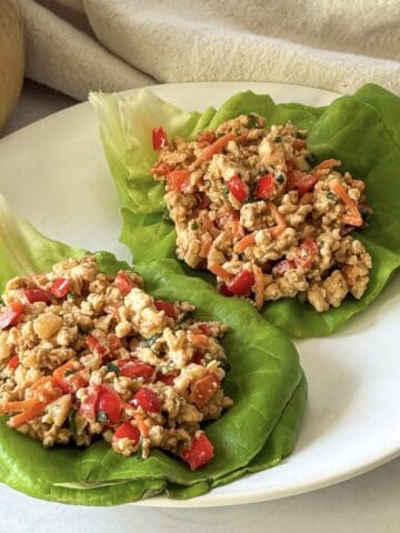 side view of 2 thai chicken lettuce wraps on a plate.